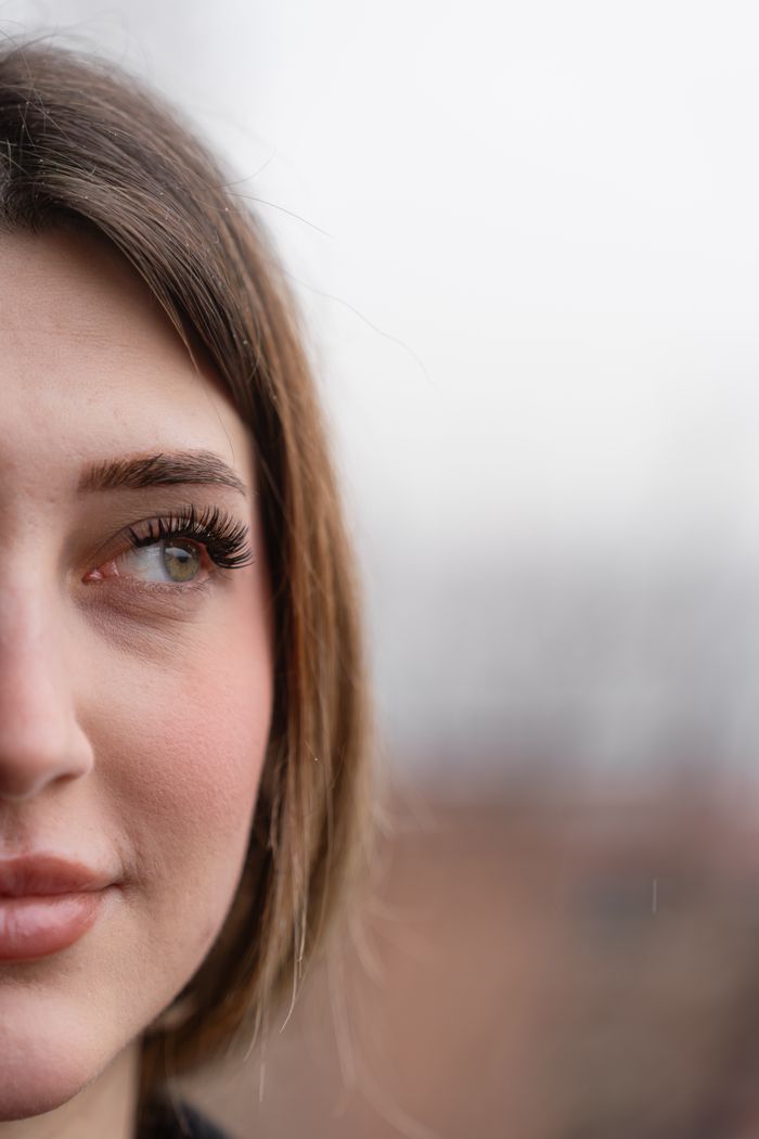 Close-up of a young woman's face, outdoors on a cloudy day, with a soft, natural look.