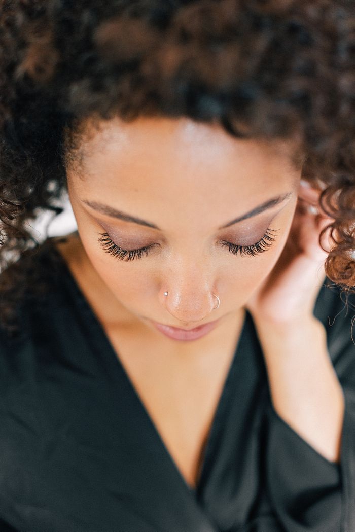 Intimate close-up of a woman with curly hair and nose piercings, eyes closed.